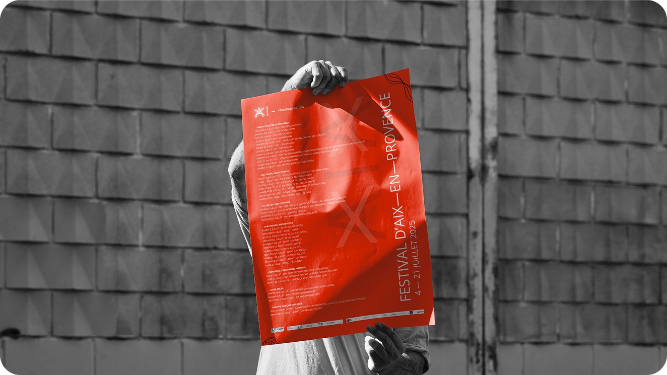Affiche du Festival d'Aix-en-Provence, rouge, tenue en main devant un mur